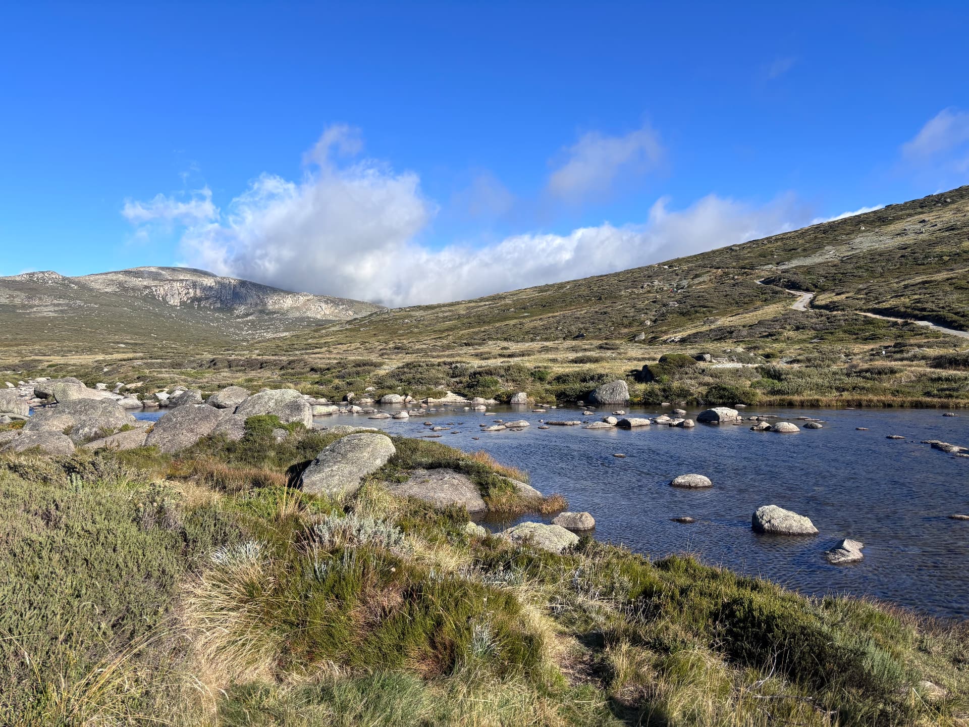 Alpine tarn among granite boulders and tussock beneath open hills