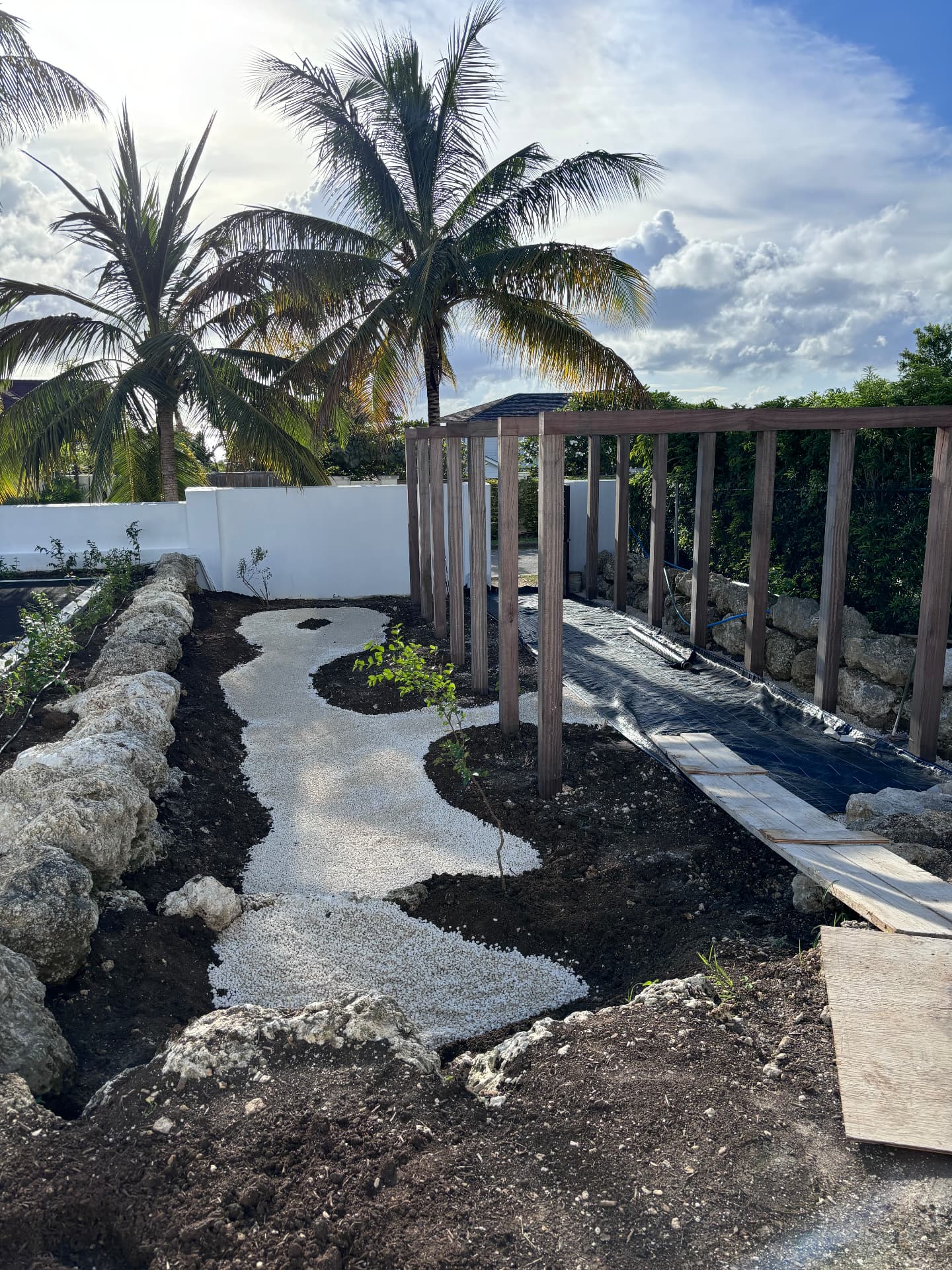 White gravel path curving between coral stone boulders under a new pergola frame