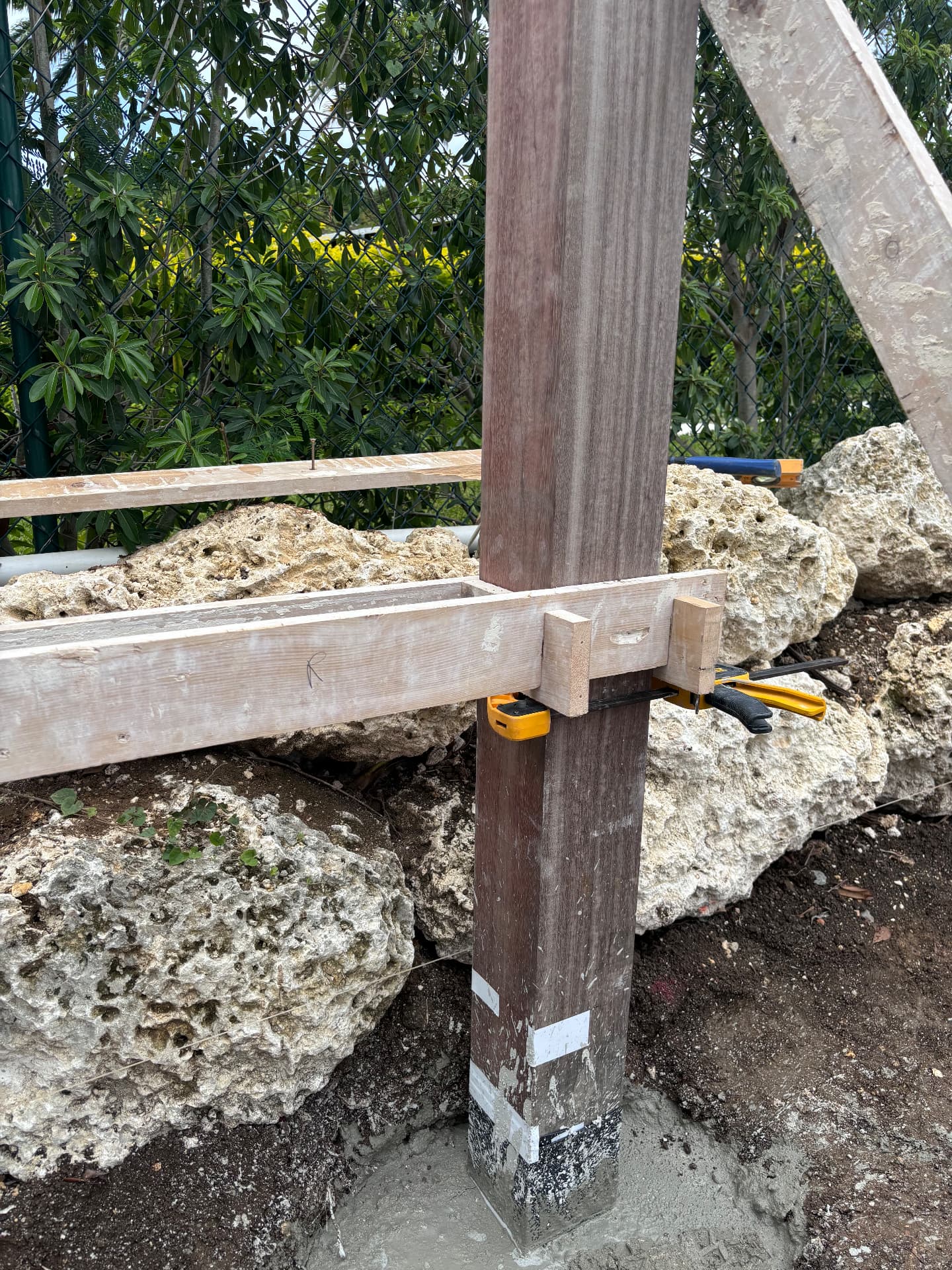 Purpleheart post braced against coral stone during pergola build