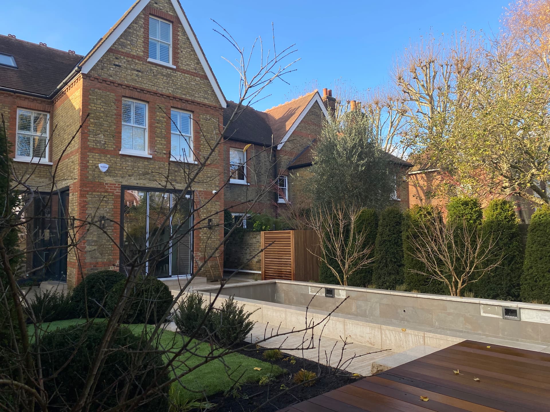 Completed London garden with clipped hedging, olive tree and stone-clad raised pool