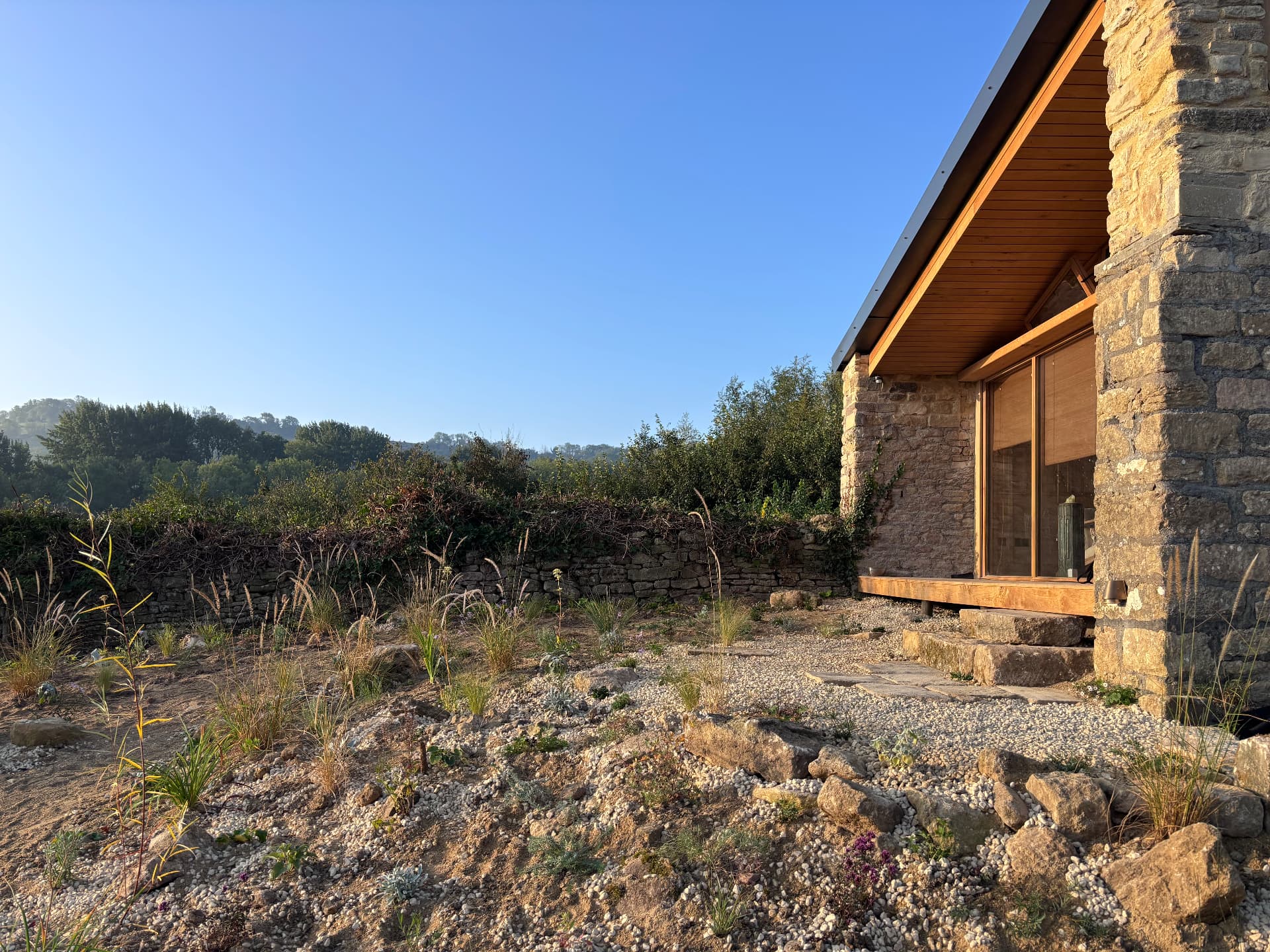Wide view of the gravel garden with drystone wall and stone steps to the studio at Studio Garden, Somerset