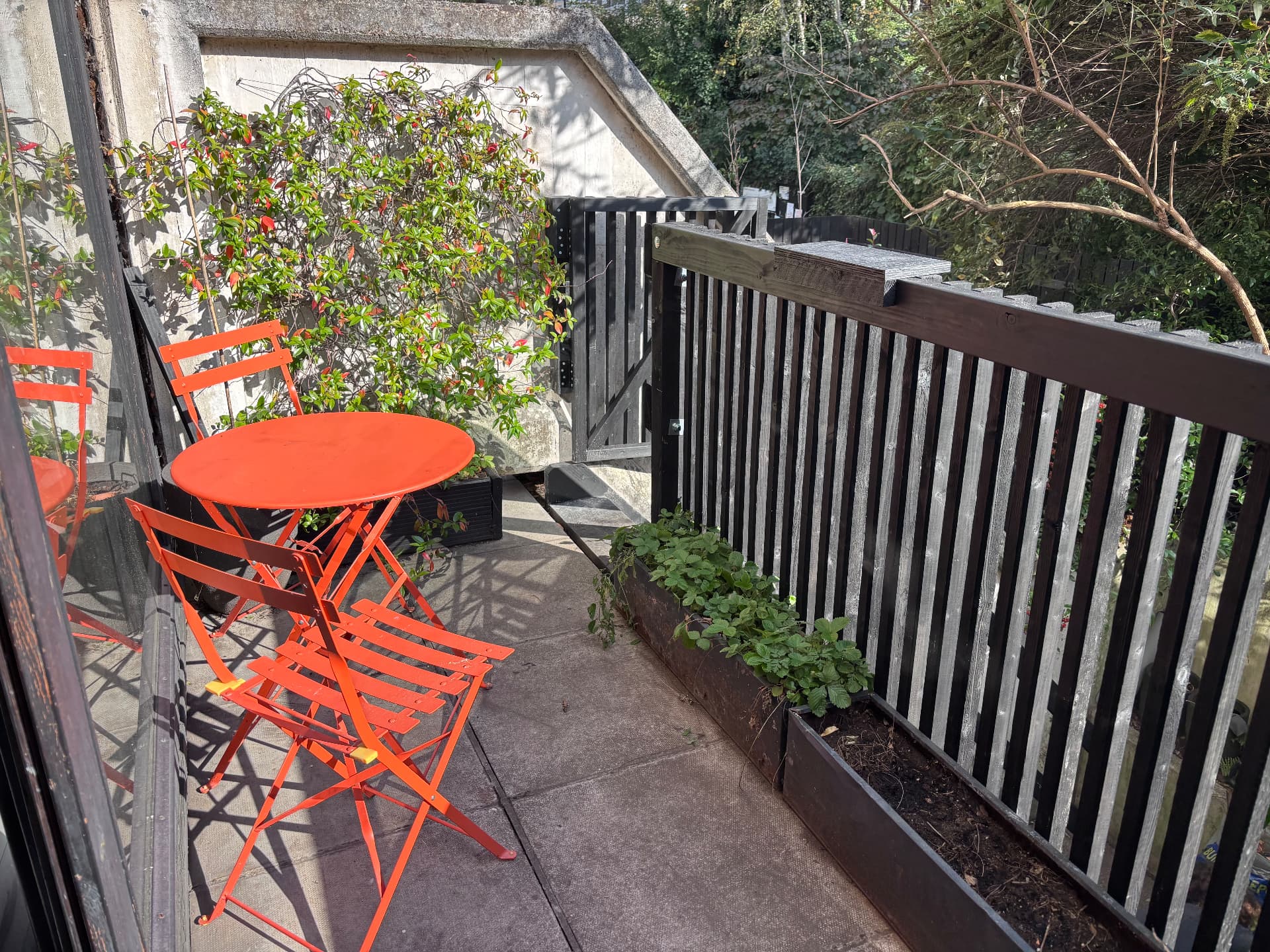 Orange bistro table and chairs on a balcony with strawberries in a steel trough