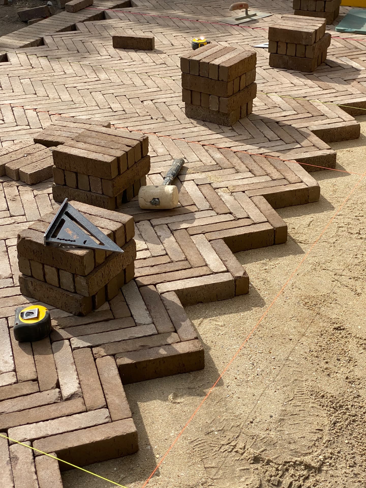 Reclaimed brick herringbone paving being laid to string lines on sand