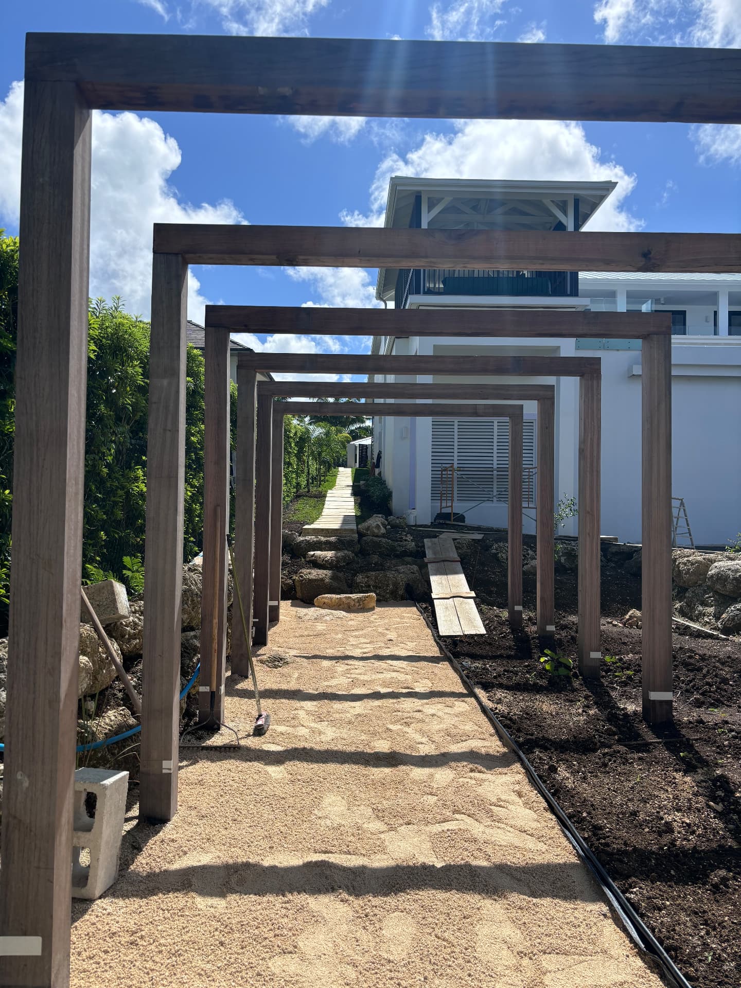 Hardwood pergola arches over a gravel walkway beside the white villa