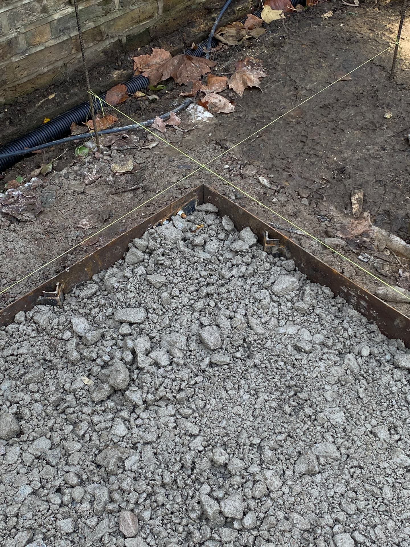 Steel edging set out with string lines over compacted hardcore against a brick wall